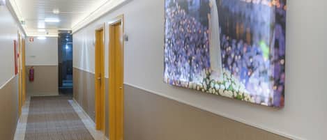 Un pasillo con piso alfombrado, puertas de madera y una obra de arte grande, colgada en la pared, que representa una escena floral.