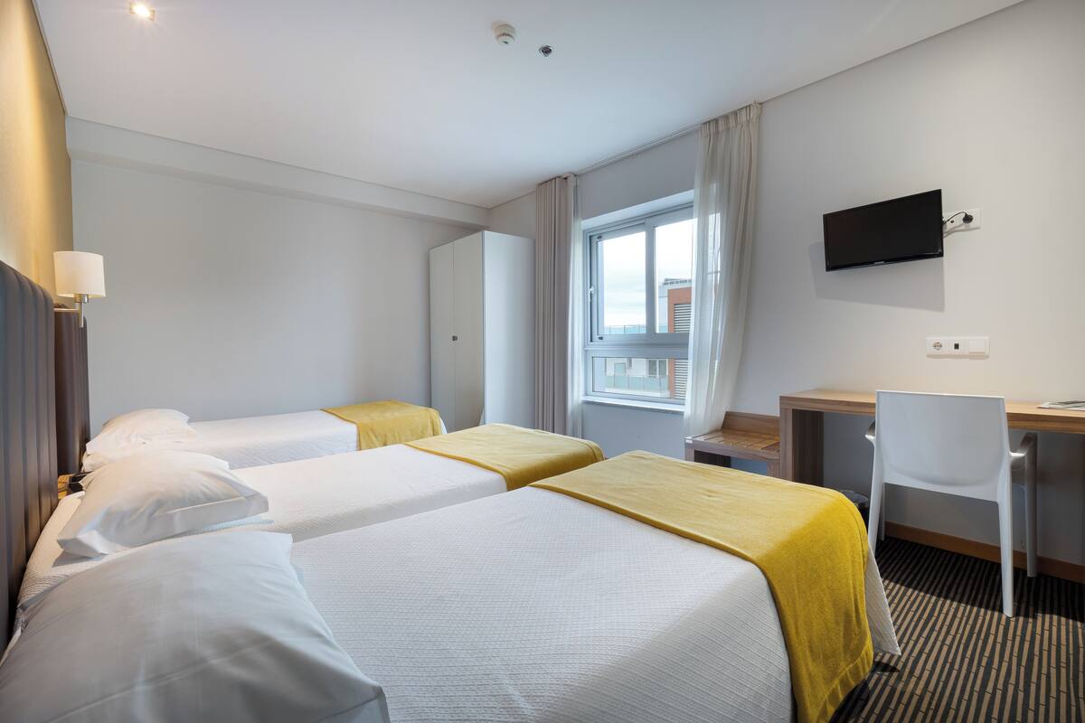 A hotel room with two beds, a desk, a chair, a television, and a window with curtains.