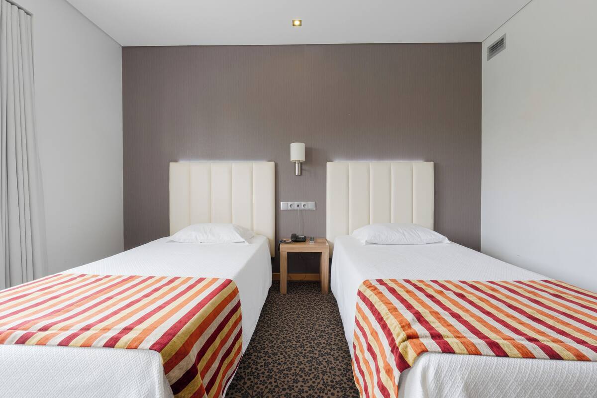 A hotel room with two beds, a nightstand, and a lamp.