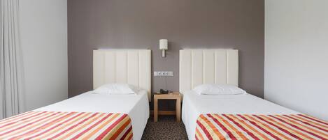 A hotel room with two beds, a nightstand, and a lamp.