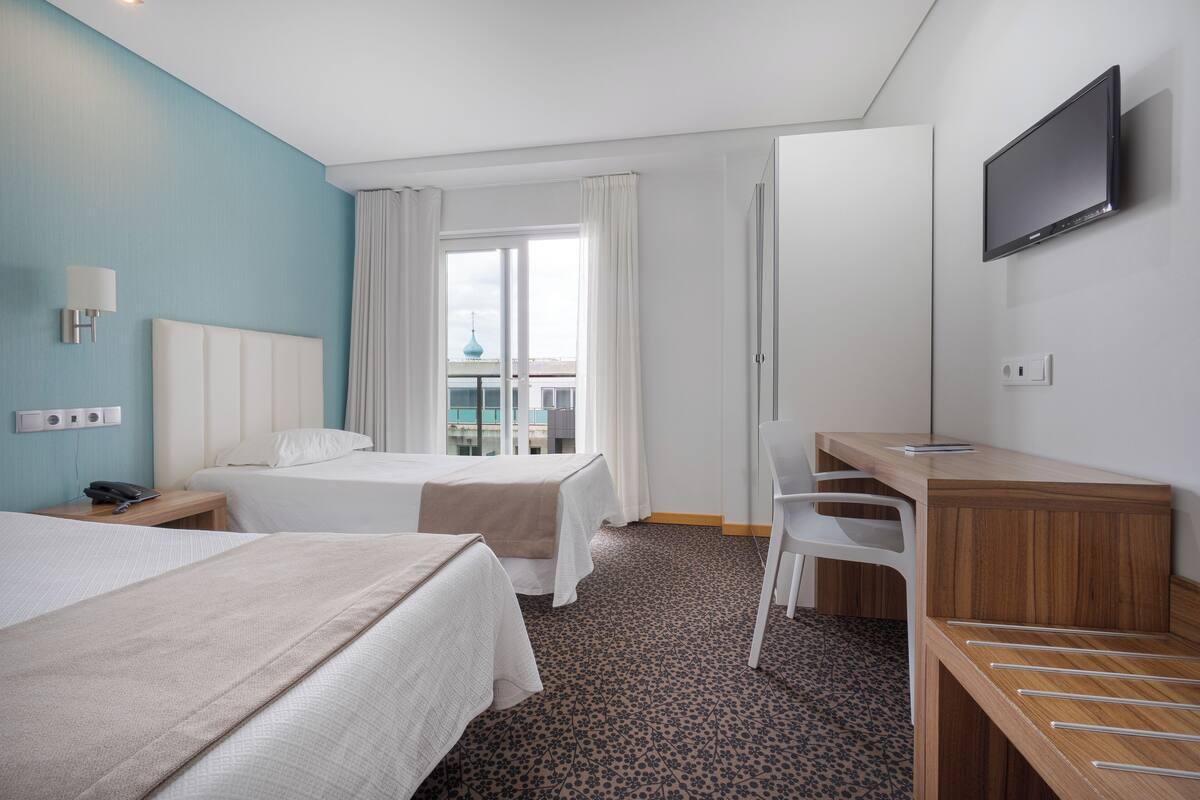 A hotel room with two beds, a desk, a chair, a TV, and a window with curtains.
