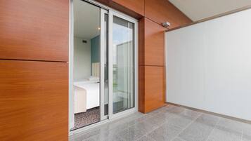 Una habitación moderna con puerta de vidrio corredera que da a un balcón, una cama y una pared blanca.