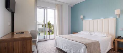 A hotel room with a bed, a desk, a chair, a TV, and a view of the outdoors.
