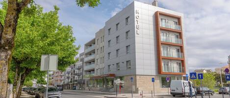 A modern hotel with a white facade and brown accents, featuring multiple floors and balconies.