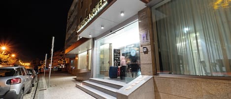 A hotel entrance with a modern design, featuring a glass facade, a staircase leading to the entrance, and a well-lit exterior.