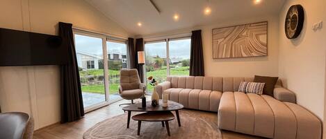 A modern living room with a sofa, armchair, coffee table, and a view through large windows.