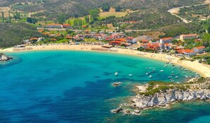 Vista aerea di una cittadina costiera con una spiaggia sabbiosa curvata, acque cristalline turchesi e numerose imbarcazioni.