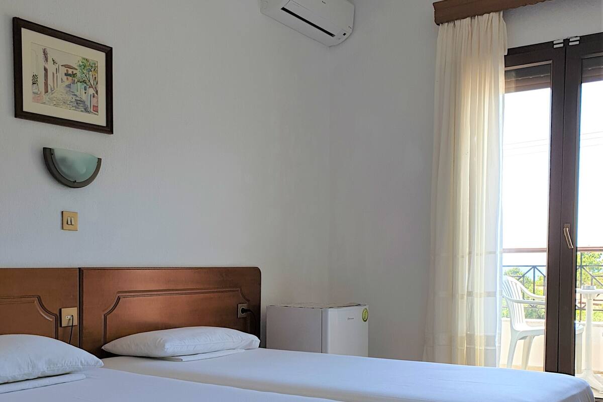 A hotel room with two beds, a small air conditioning unit, a wall-mounted light fixture, and a window with curtains.