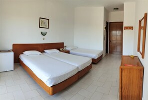 A hotel room with two single beds, a wooden headboard, a bedside table with a lamp, a small desk, and a mirror on the wall. - Ermioni Hotel (Sithonia)