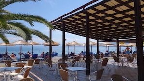 A beachside café with outdoor seating, umbrellas, and a view of the sea. - Nafsika Beach (Delphi)