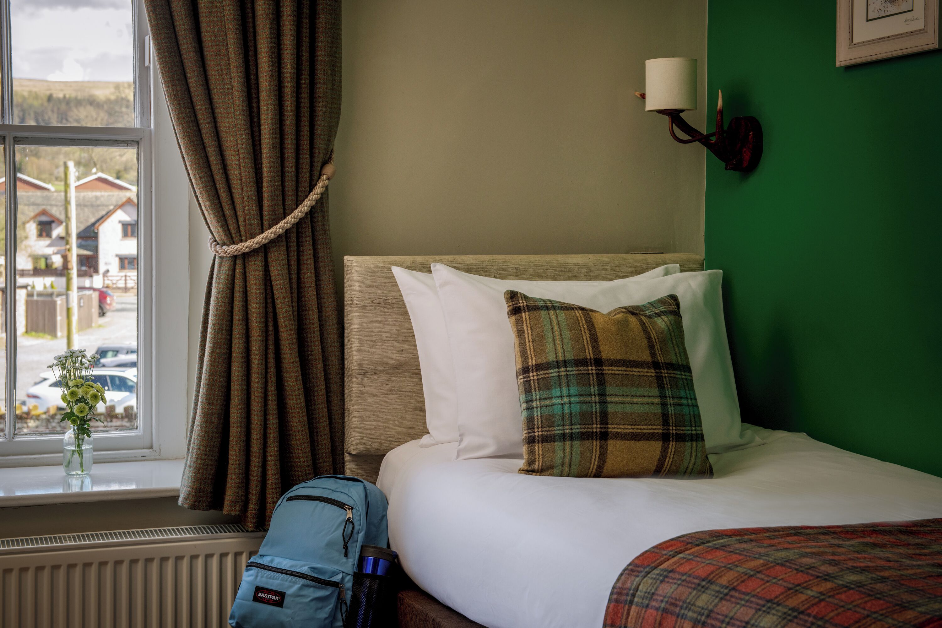 Een hotelkamer met een bed, een raam met gordijnen, een lamp en uitzicht op huizen.