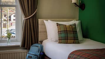 Een hotelkamer met een bed, een raam met gordijnen, een lamp en uitzicht op huizen.