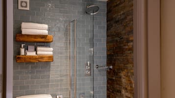 A modern bathroom with a glass-enclosed shower, a wooden shelf with towels, and a blue-tiled wall.