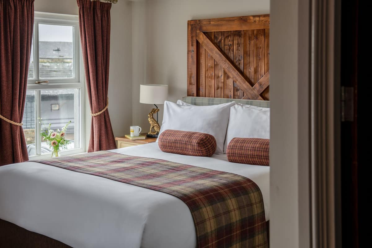A neatly made bed with a plaid bedspread, a wooden headboard, and a bedside table with a lamp and a decorative item.
