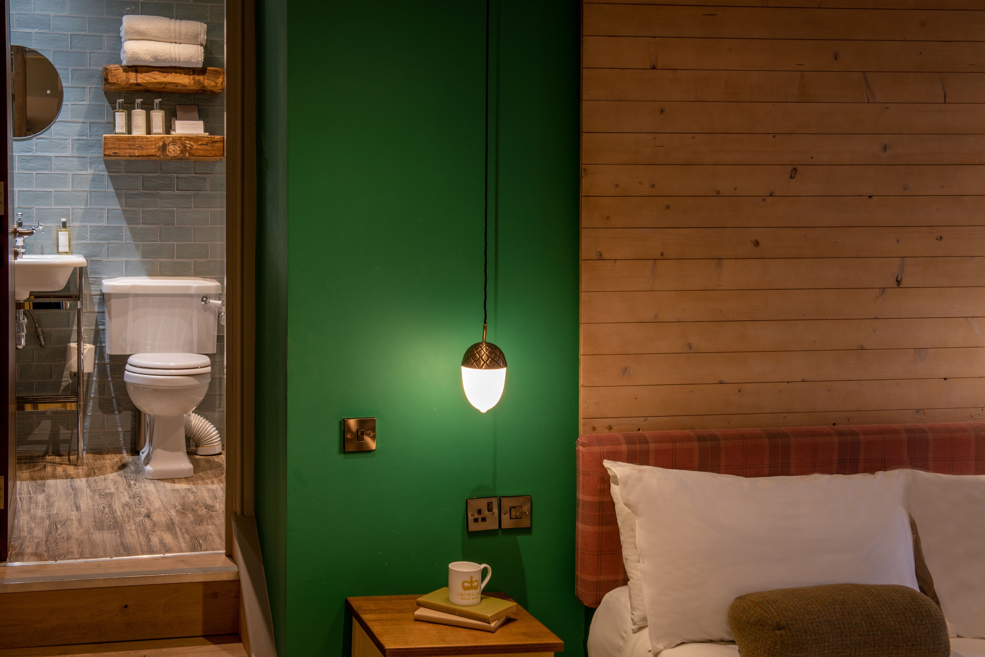 A bathroom with a green wall, wooden floor, and a wooden bench with a white pillow.