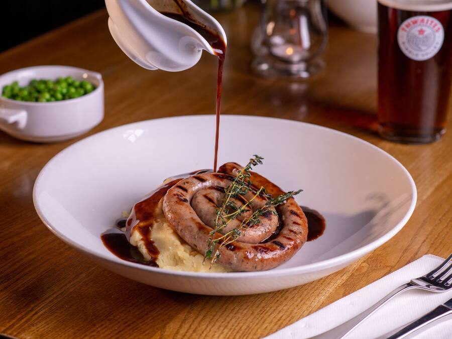 A plate with a sausage, mashed potatoes, and gravy.