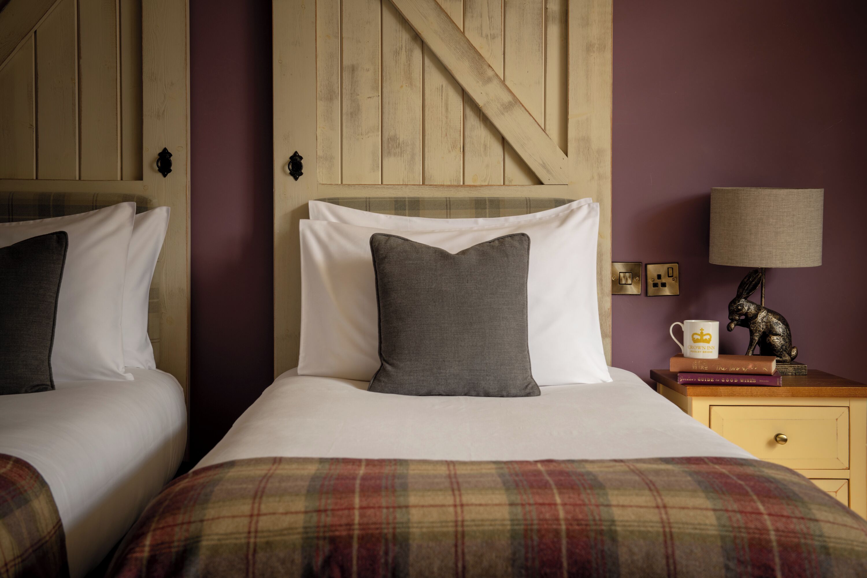 A bedroom with two beds, a wooden headboard, a nightstand with a lamp, and a decorative statue.