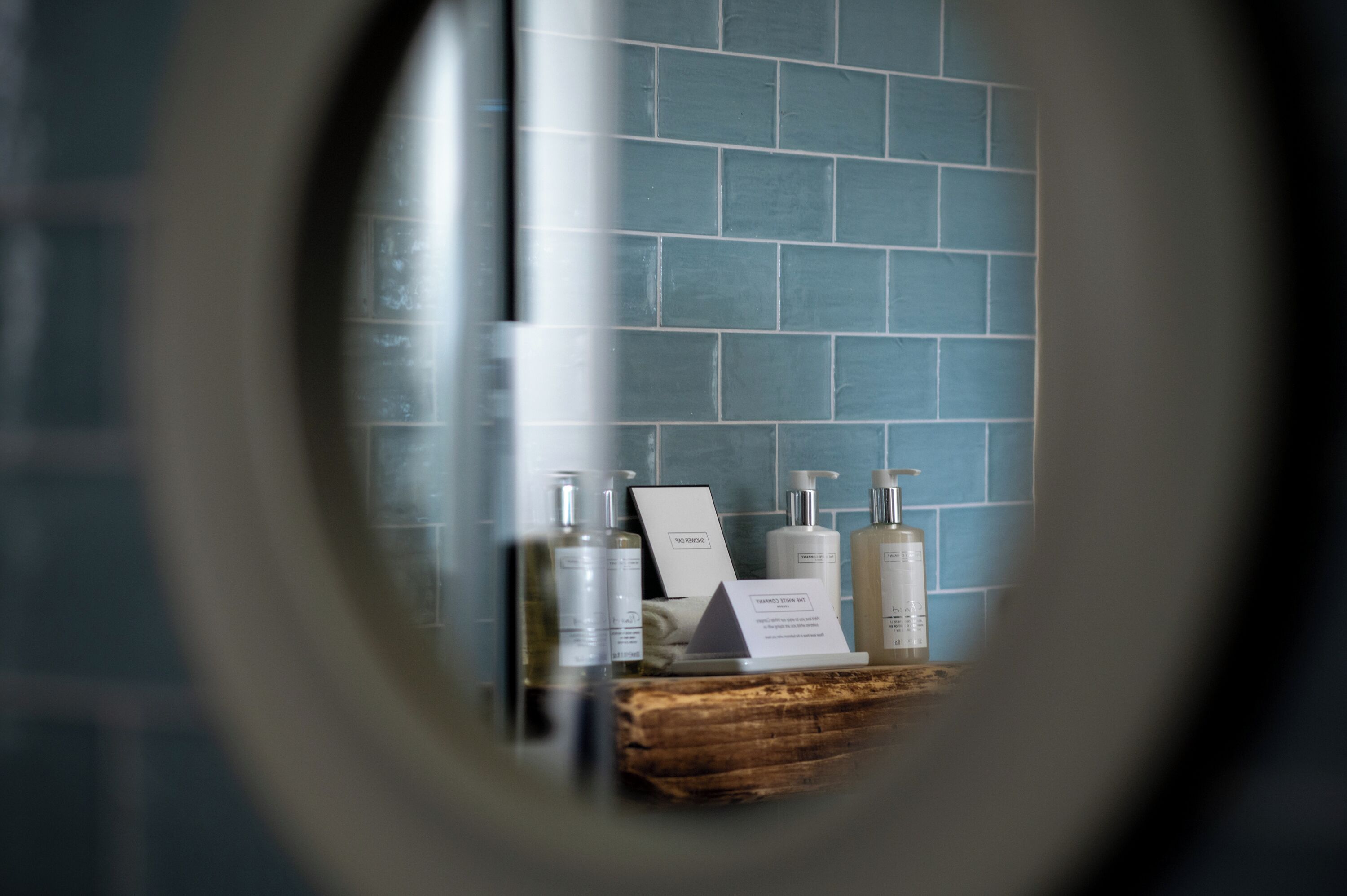 Ein Badezimmer mit blauen Fliesen, einem Holzlager und Pflegeprodukten, darunter eine Shampooflasche, eine Spenderflasche für Conditioner und ein Seifenspender.