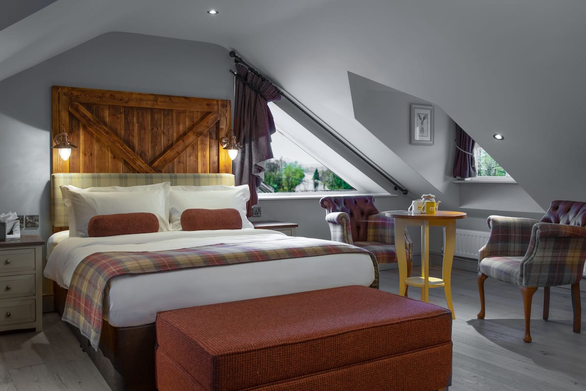 A bedroom with a large bed, a wooden headboard, a small table with a lamp, and a window with curtains.