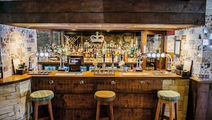A bar with a wooden counter, stools, and a variety of bottles and glasses. - Crown Inn at Pooley Bridge (Penrith)