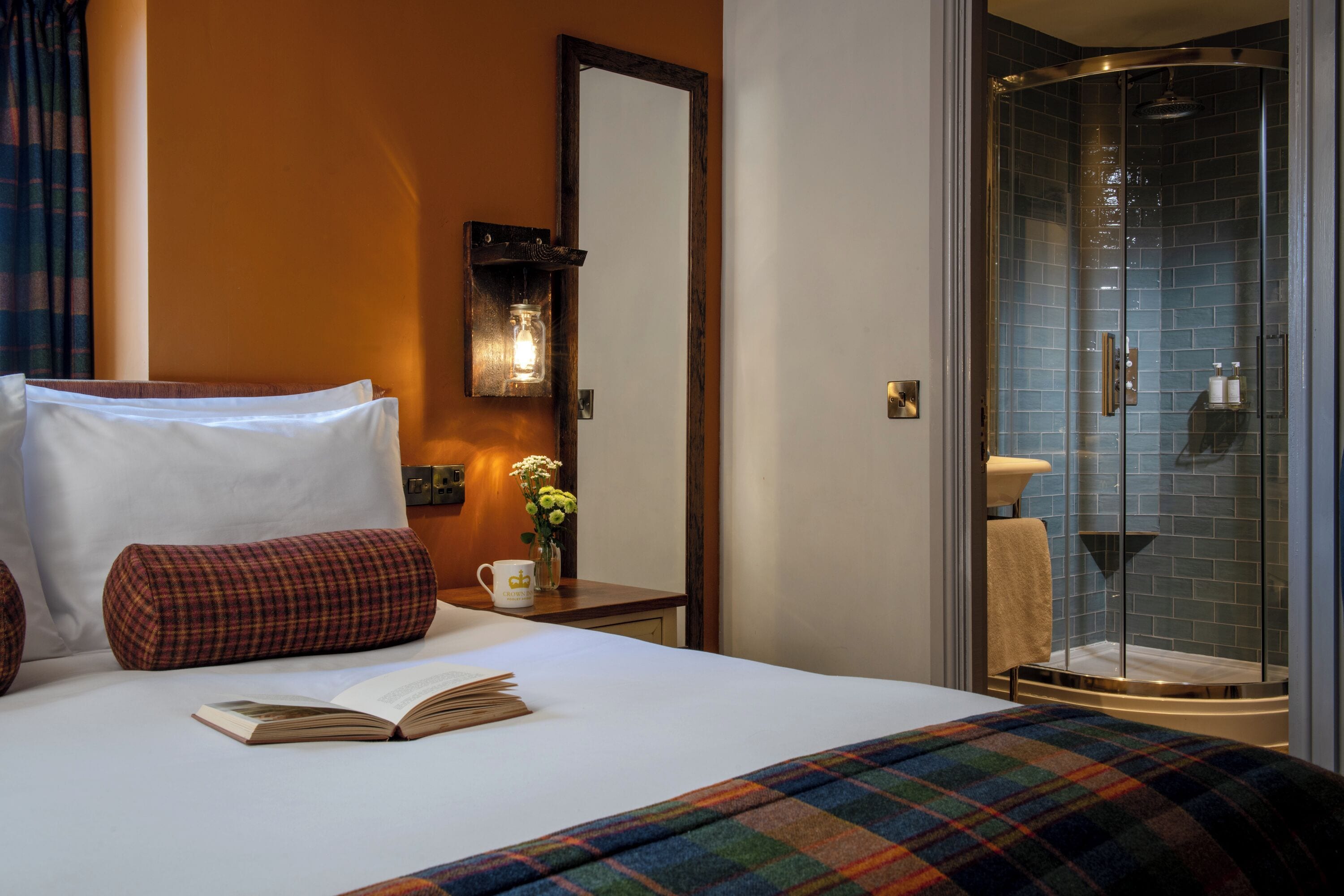 Hotelkamer met een bed, nachtkastje met een boek en mok, spiegel en douche met glazen deuren.
