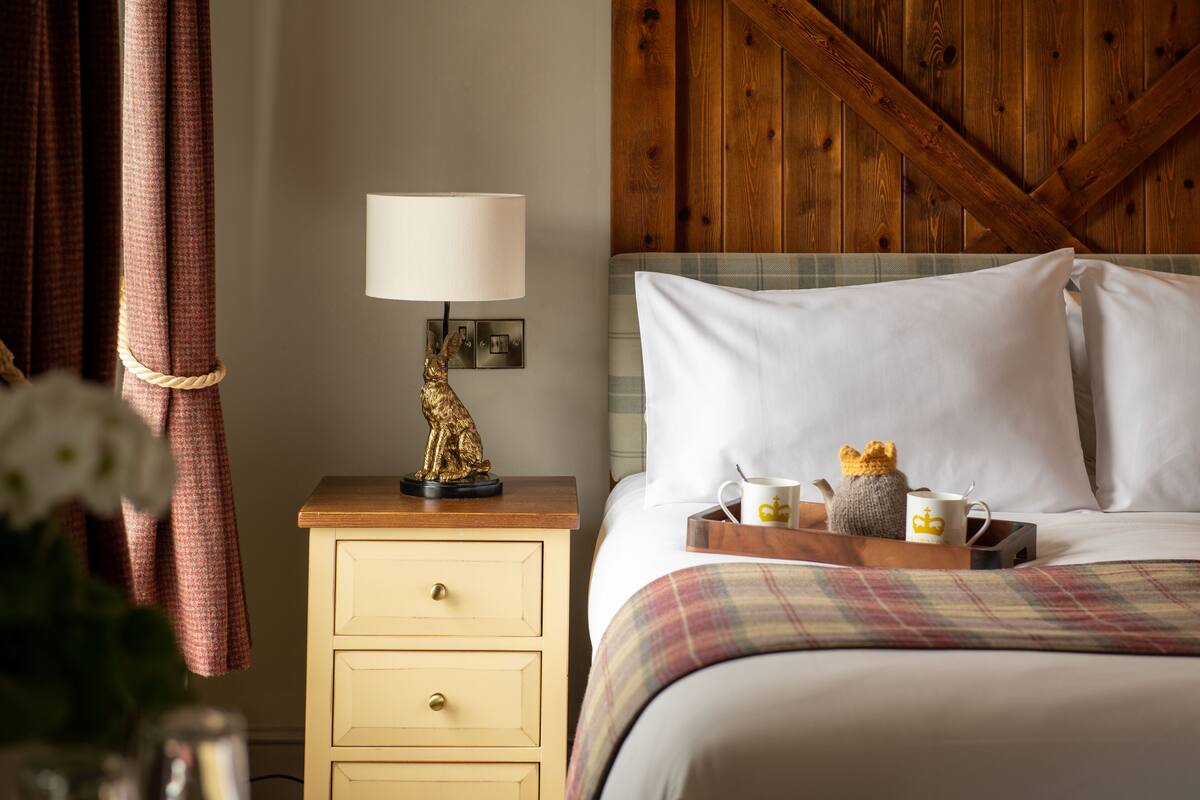 A neatly made bed with white pillows and a plaid blanket, a bedside table with a lamp and decorative items, and a wooden wall panel.