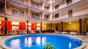 Una piscina interior con un área de estar central, varios balcones y una zona de comedor con mesas y sillas.