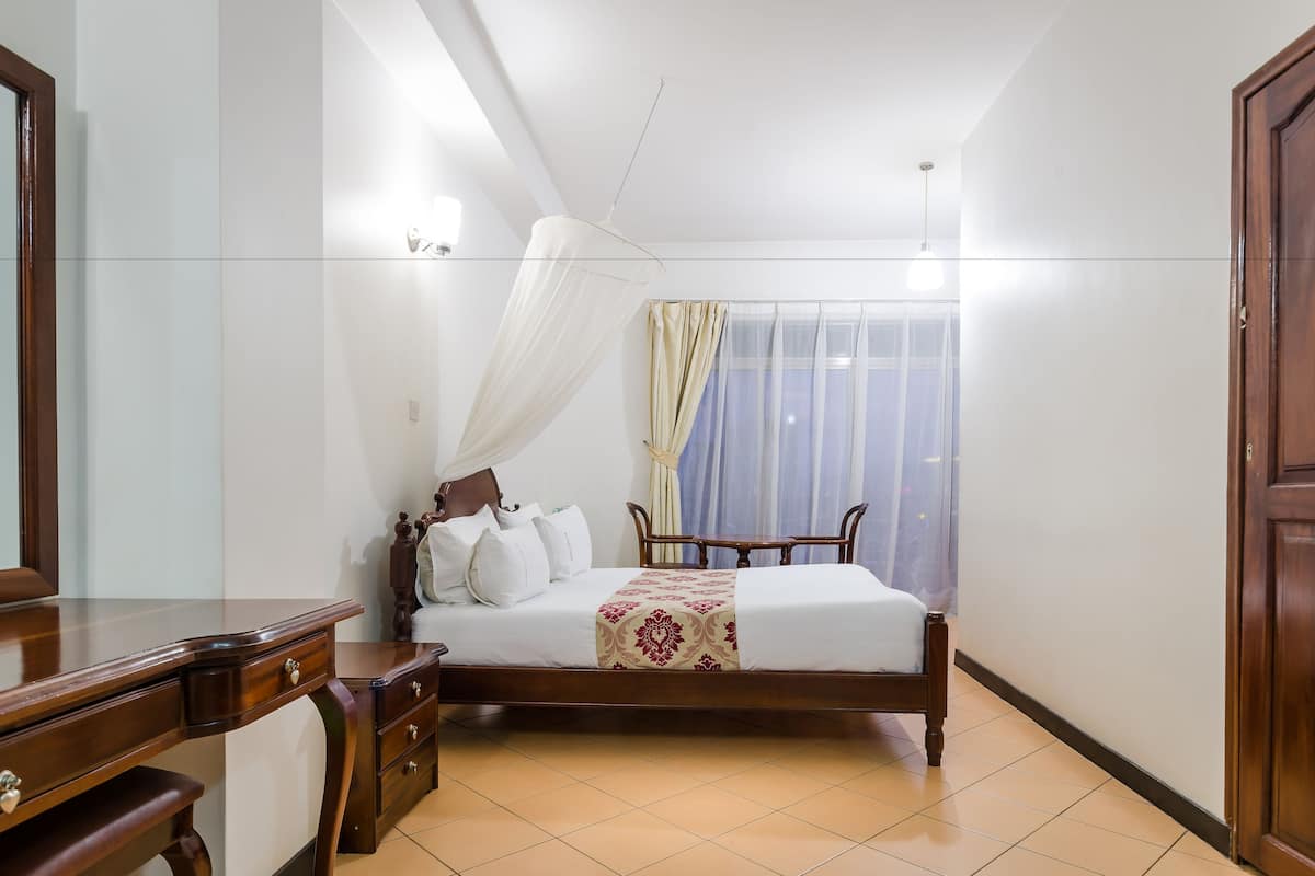 A bedroom with a wooden bed, a bedside table, a mirror, and a window with curtains.