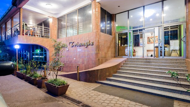 Entrada de un hotel con un llamativo letrero 'Triangle', un mostrador de recepción y una escalera que conduce al acceso.