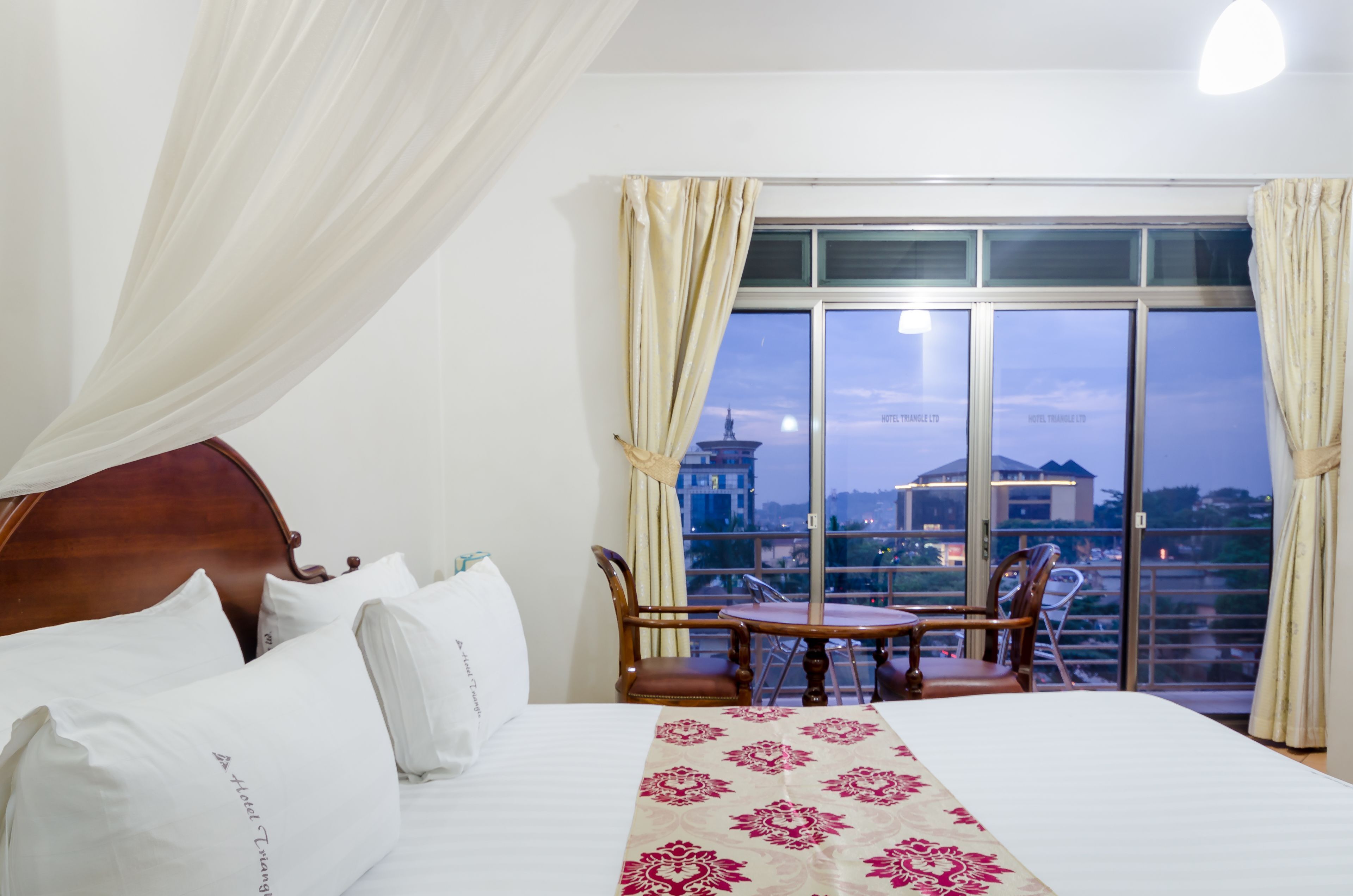 Habitación de hotel con una cama grande, una mesa de comedor con sillas y un balcón con vistas a la ciudad.
