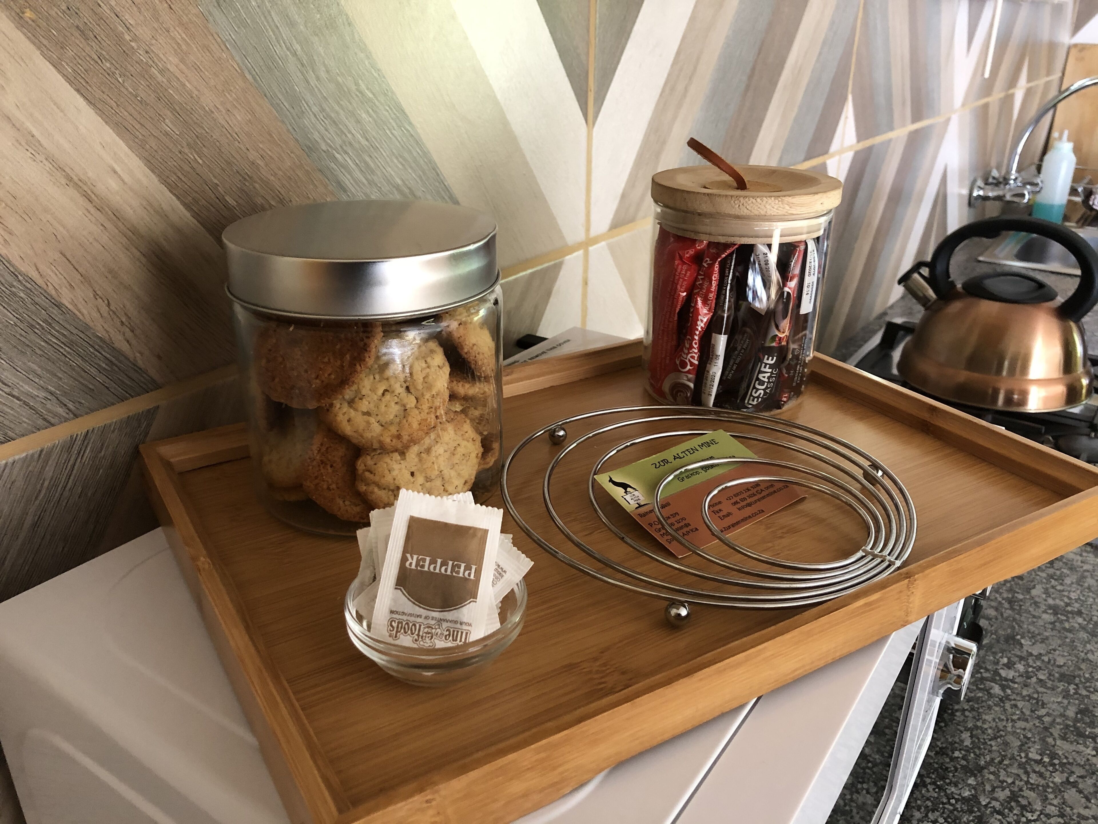 A tray with a jar of cookies, a container of tea, and a packet of sugar cubes.
