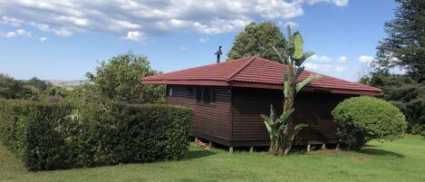 Una cabaña de madera con techo rojo, rodeada de exuberante follaje y un cielo azul despejado.