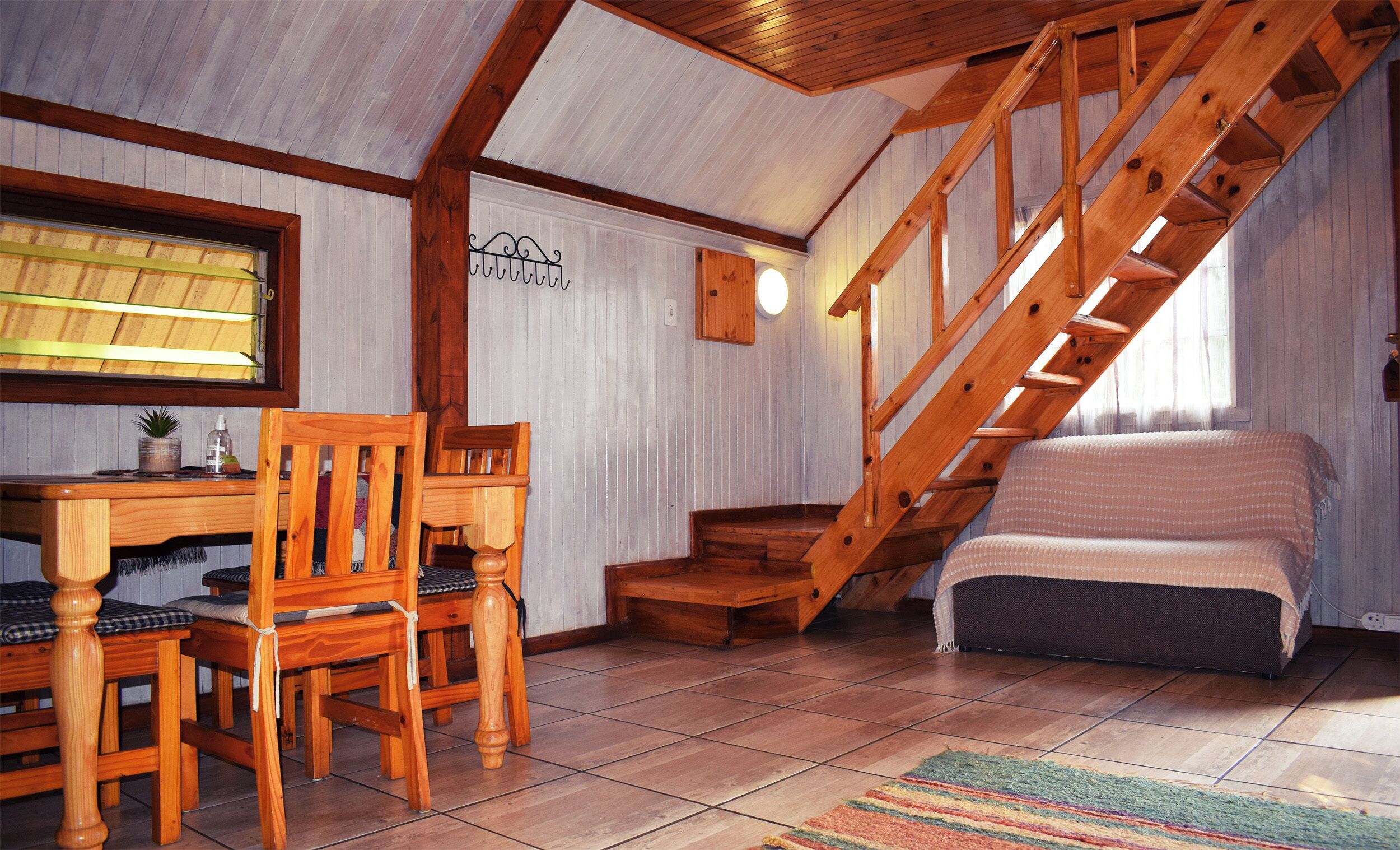 Un dormitorio acogedor en el ático con una escalera de madera, una pequeña mesa con sillas y una cama.