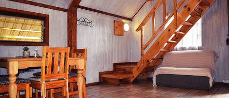 Un dormitorio acogedor en el ático con una escalera de madera, una pequeña mesa con sillas y una cama.