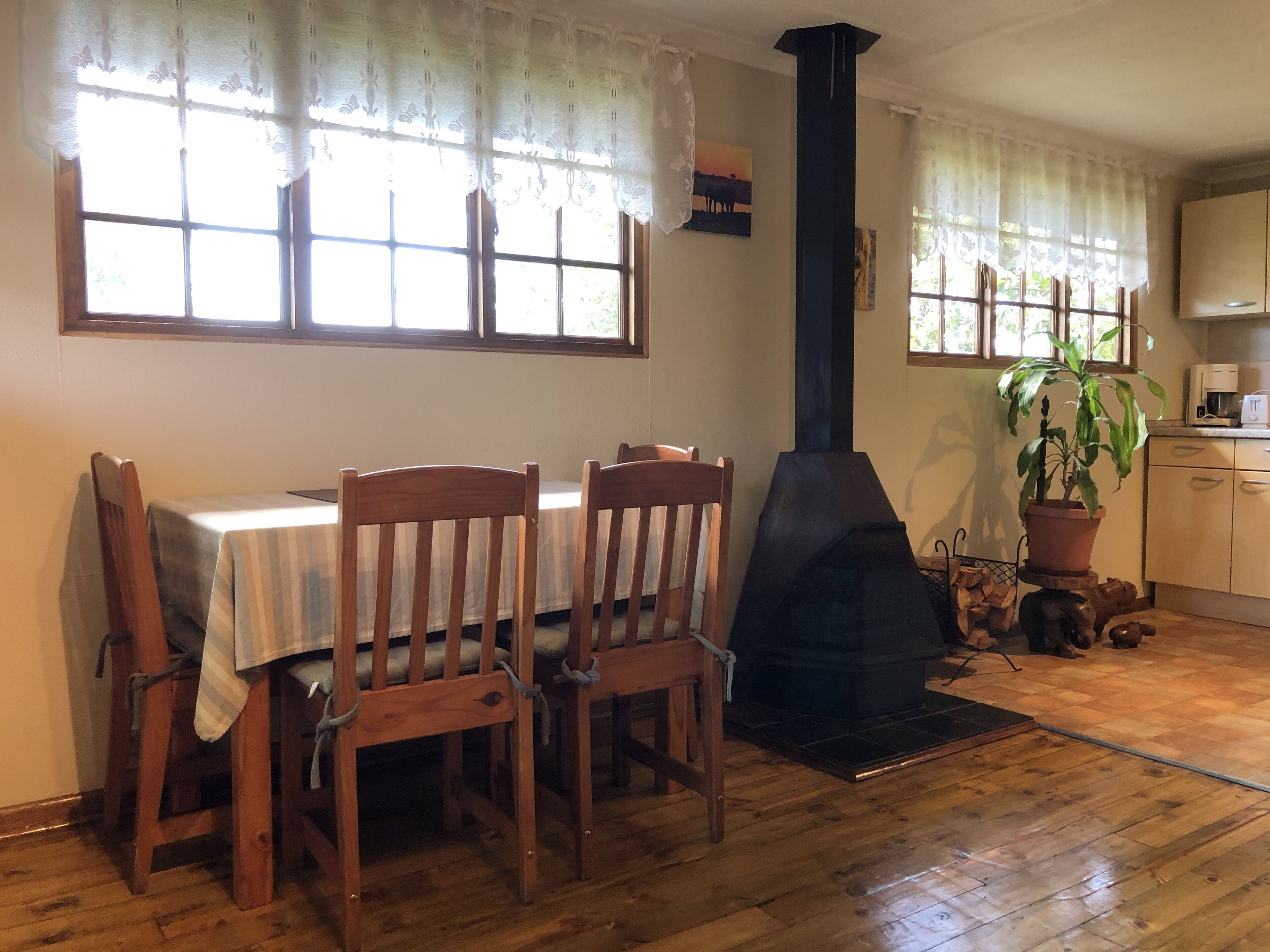 A dining area with a table and chairs, a fireplace, a window with curtains, and a kitchen area with cabinets and a potted plant.