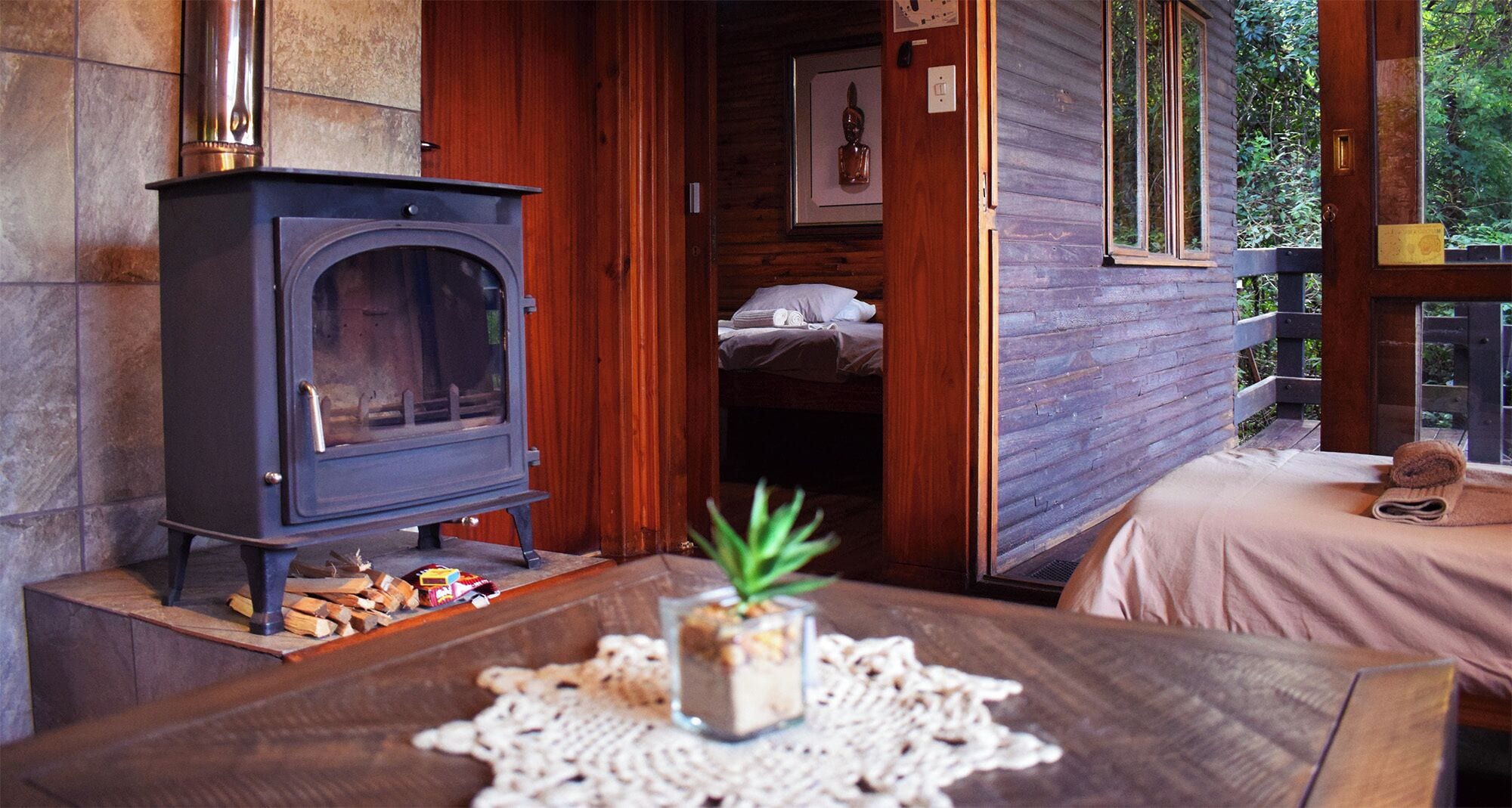Una habitación acogedora con estufa de leña, cama con vistas y una mesita con planta y aperitivos.