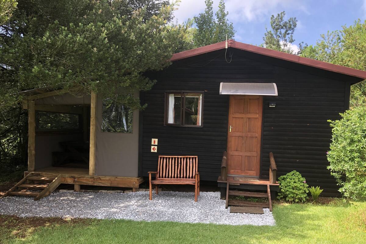 A small cabin with a wooden door, a bench, and a covered porch area.
