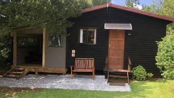 Una cabaña pequeña con puerta de madera, un banco y un porche cubierto.