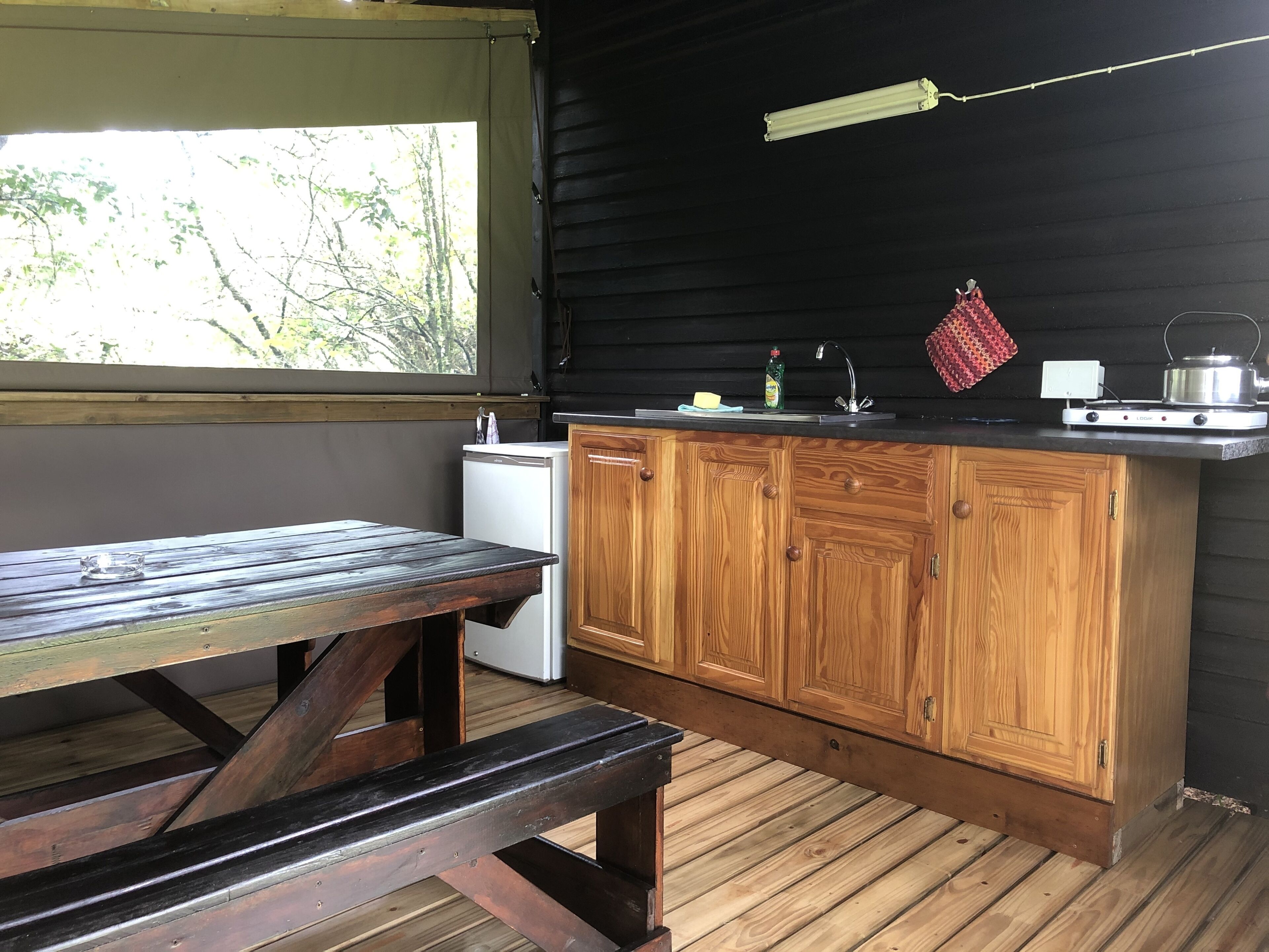 Una cocina rústica con armarios de madera, un refrigerador pequeño, una mesa de madera y una ventana con vistas a la vegetación.