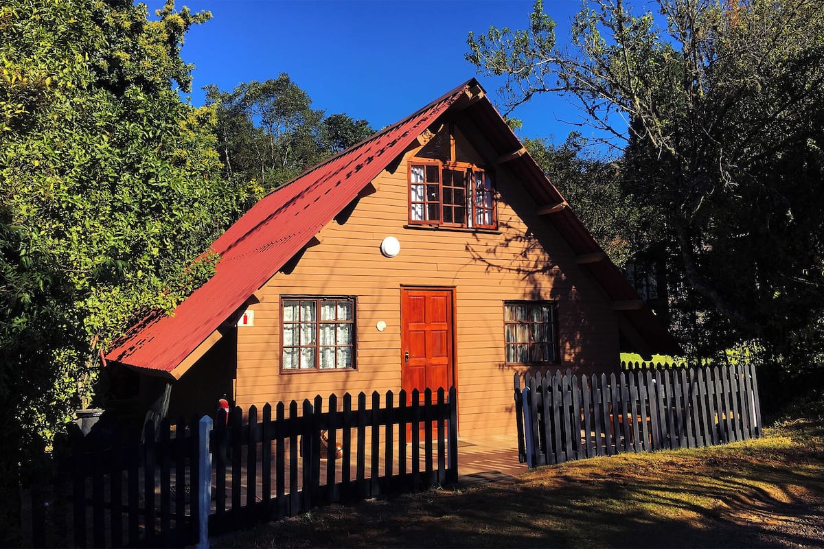 A wooden cabin with a red roof, a front door, and a picket fence.