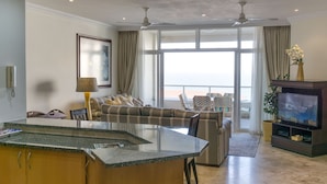 A modern living room with a large TV, a sofa, and a dining area. - 302 Oyster Schelles (Umhlanga)