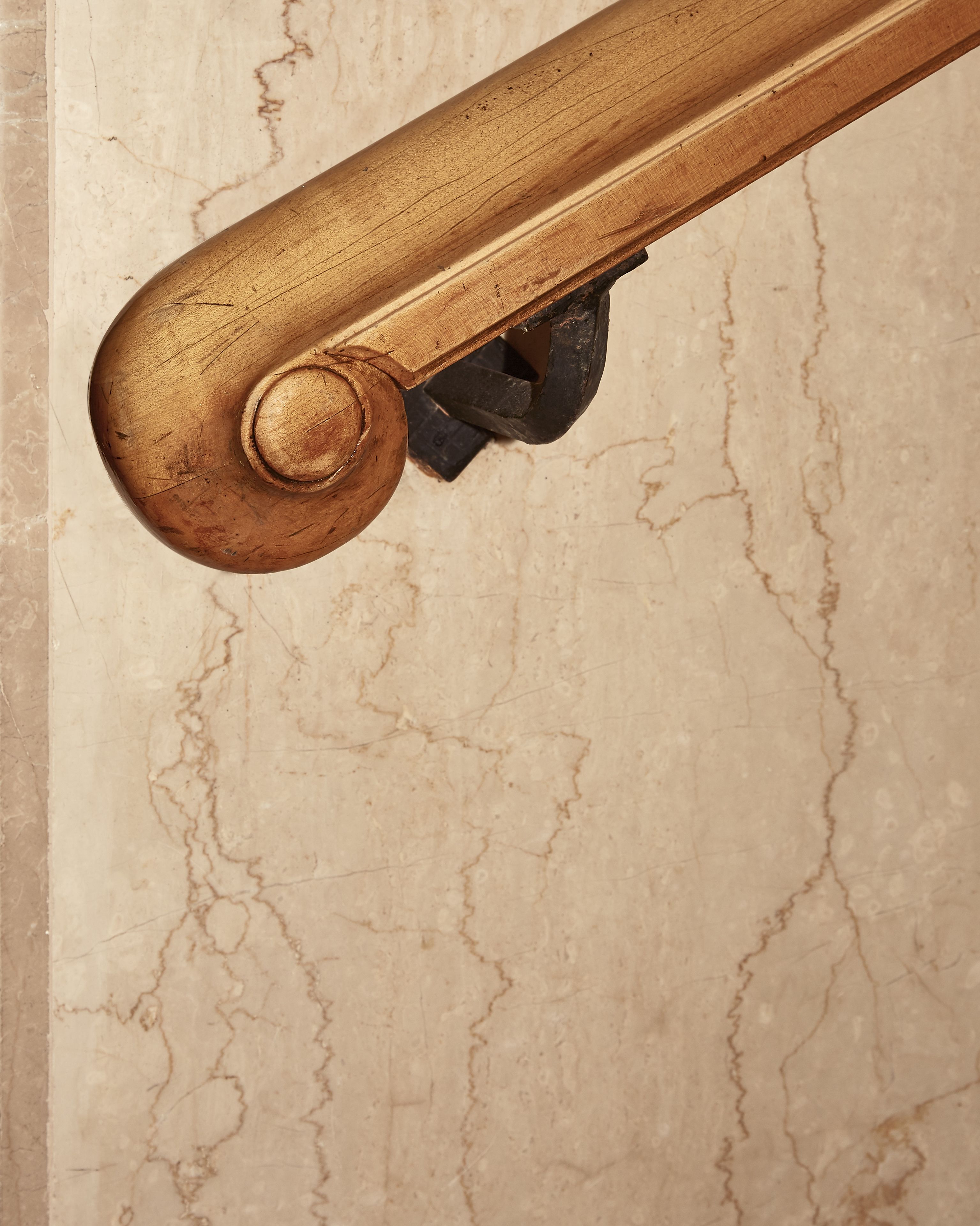 A close-up of a wooden balustrade with a curved design against a marble wall.