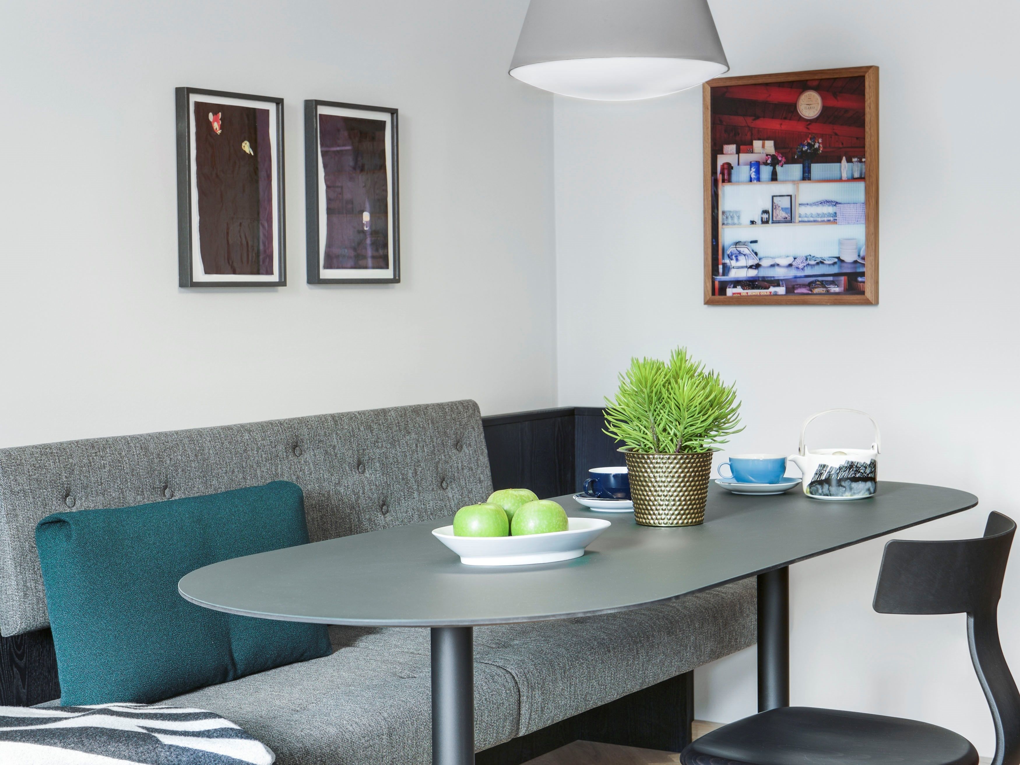 A modern dining area with a grey sofa, a round table, and a potted plant.