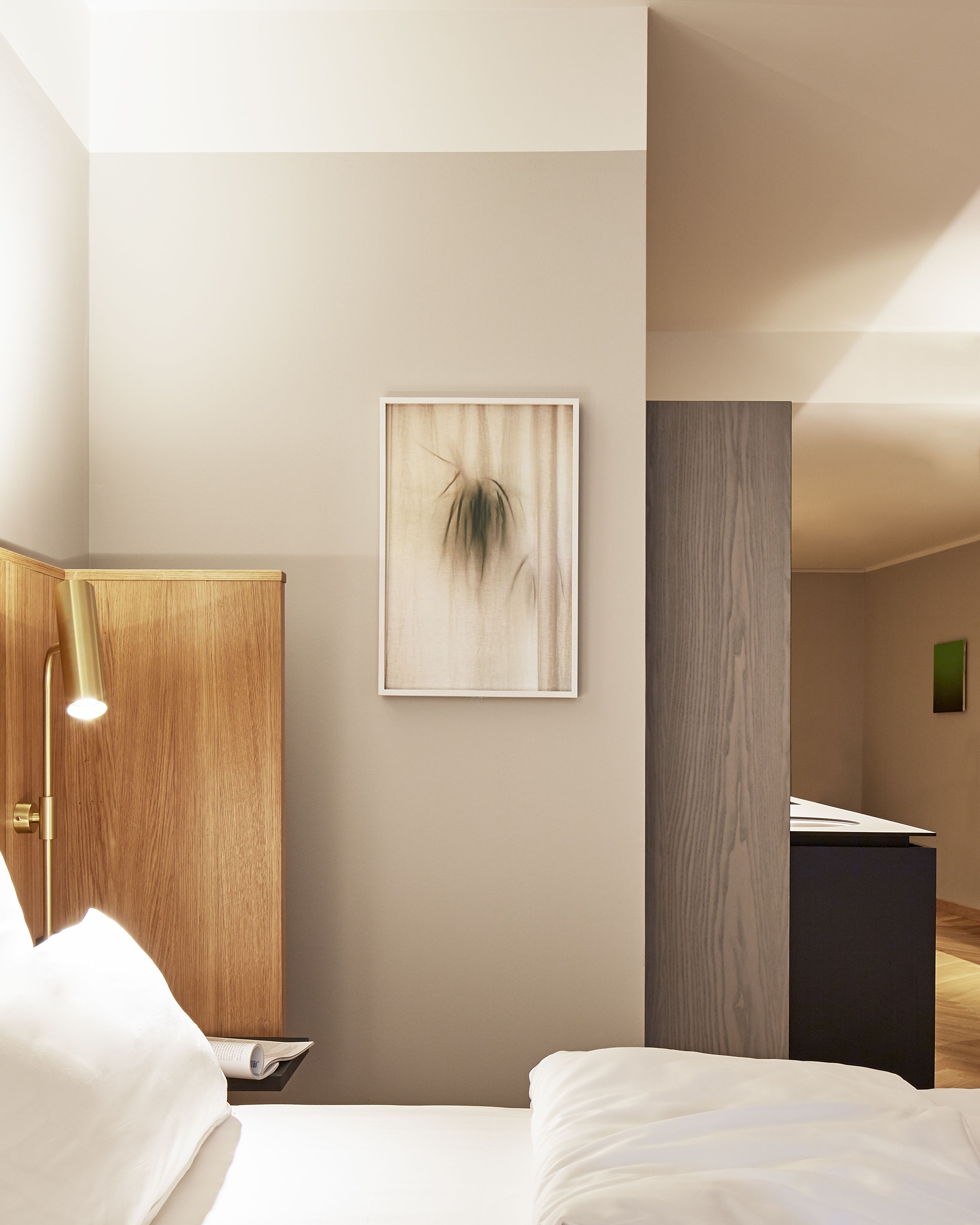 Quarto de hotel moderno com uma cama, um guarda-roupa de madeira, uma obra de arte emoldurada na parede e uma mesa com luminária.