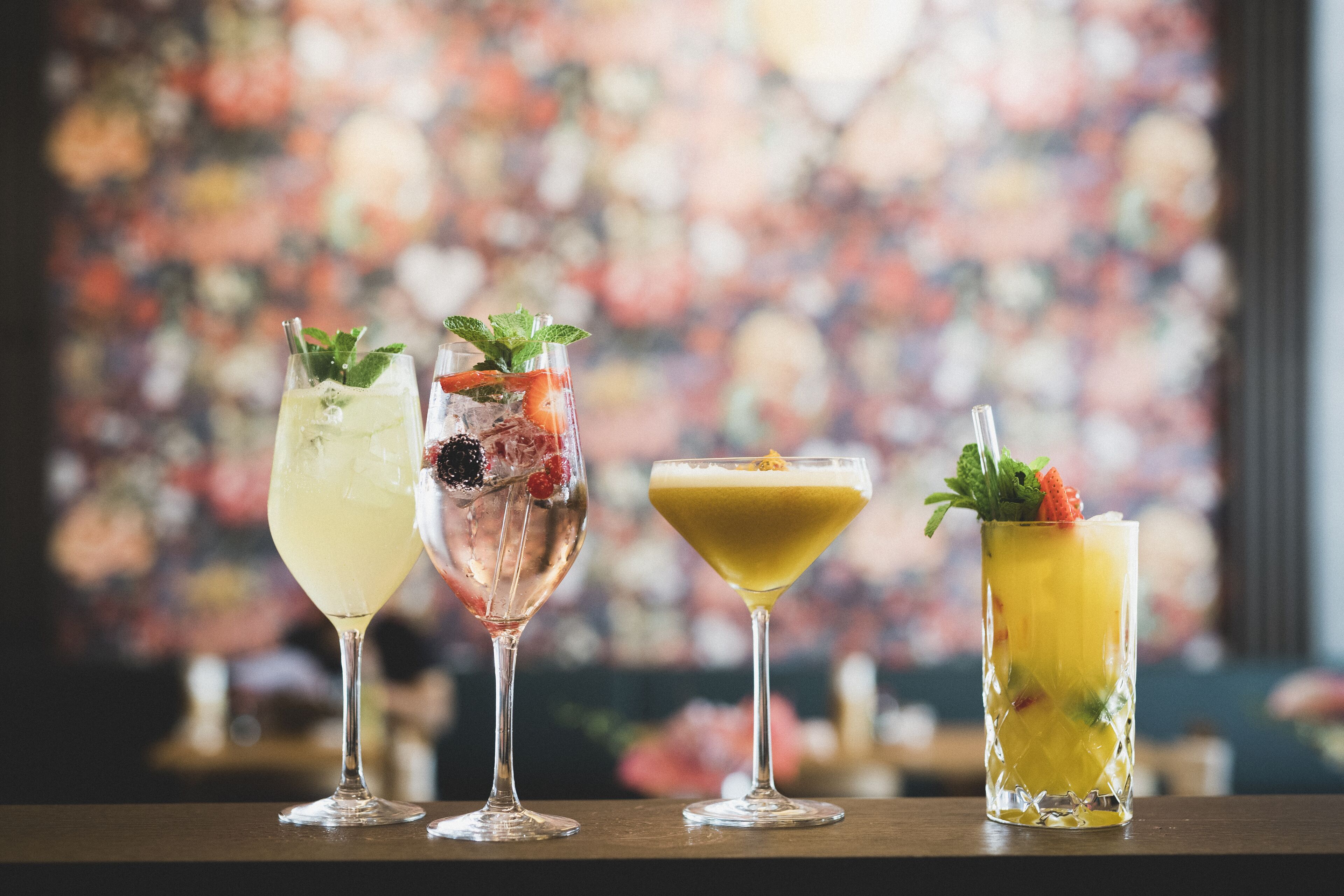 Drei Cocktails auf einer Bar, im Hintergrund florale Muster.
