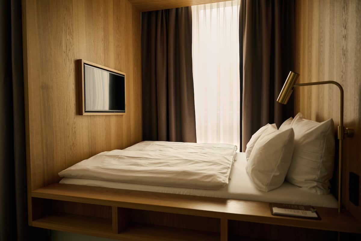 A single bed with a wooden headboard, a bedside table with a lamp, and a TV mounted on the wall.