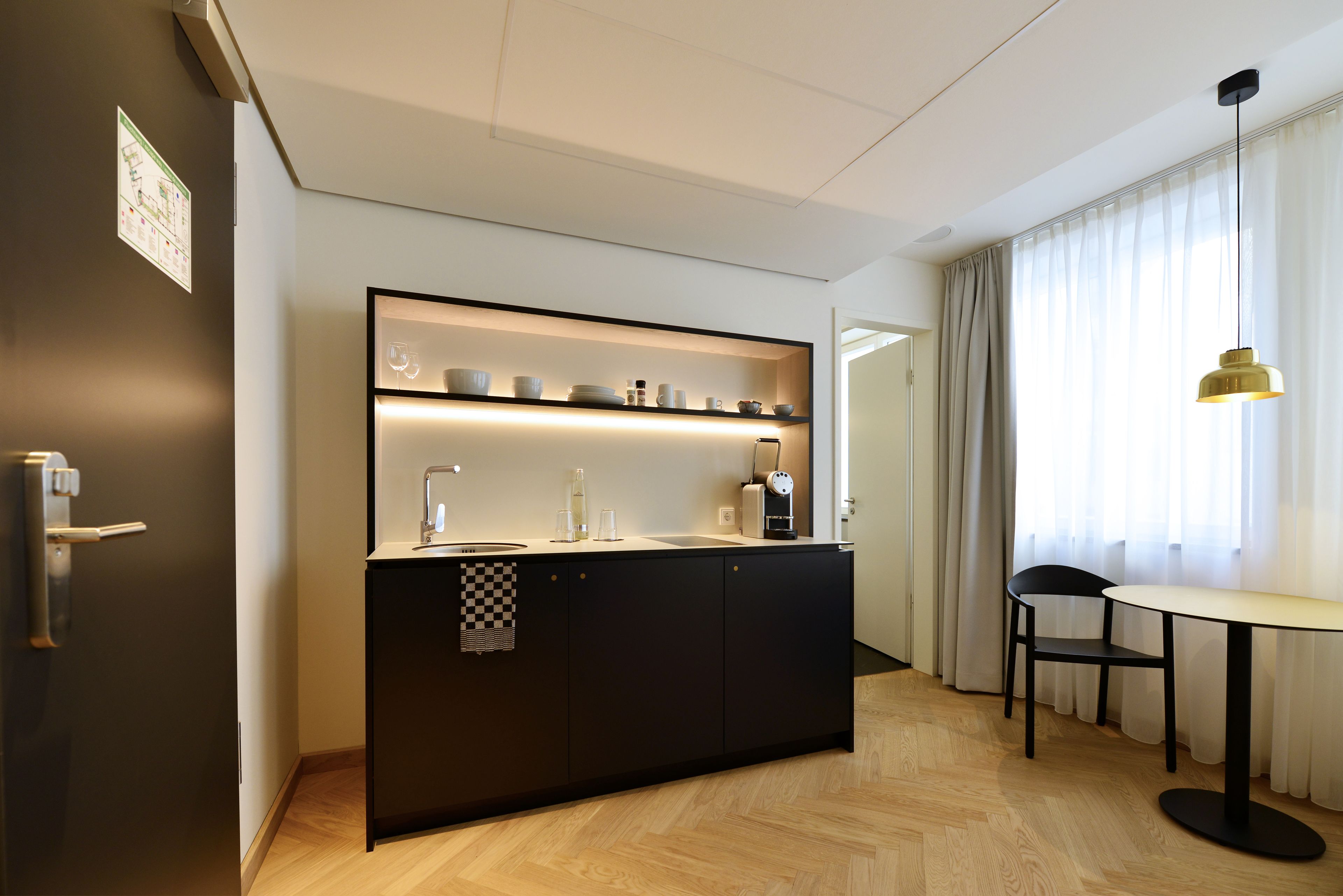 A modern kitchen with a black countertop, built-in shelves, and a small dining area with a table and chair.