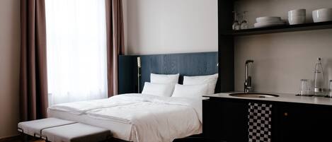 Una habitación de hotel moderna con una cama, un escritorio pequeño con lavamanos y una estantería con cristalería y vajilla.
