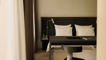 A hotel room with a bed, a desk, a chair, a lamp, and curtains.