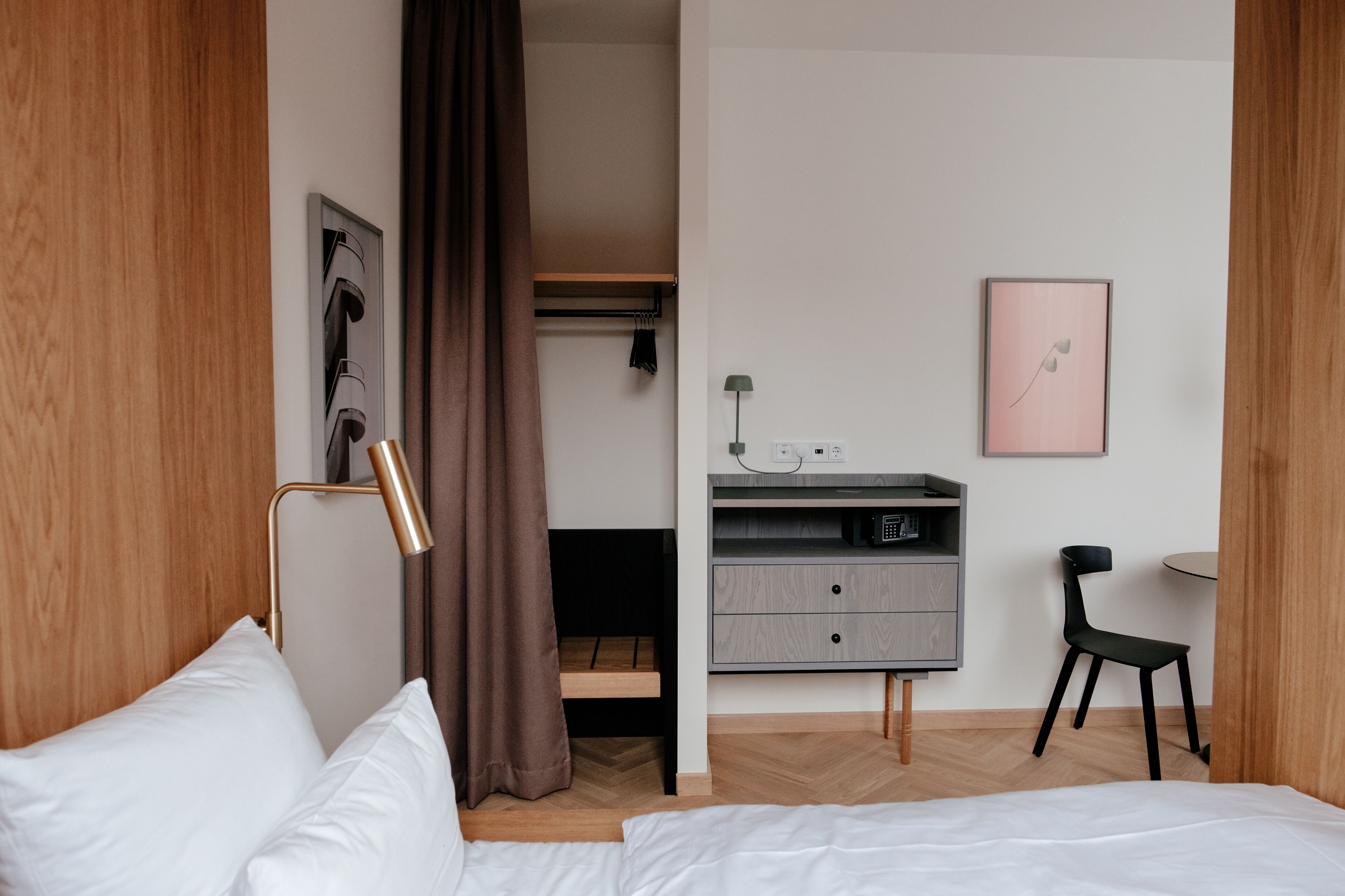 A modern hotel room with a bed, a desk, a chair, and a wardrobe.